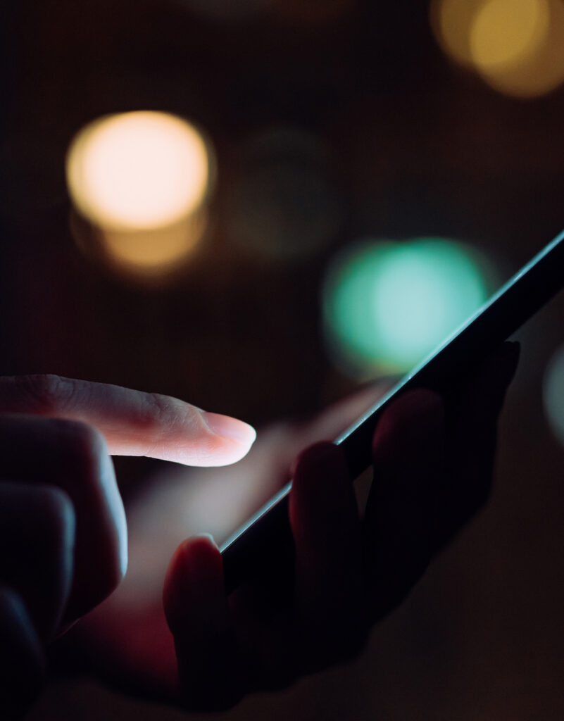 Close up of woman's hand using smartphone in the dark, against illuminated city light bokeh